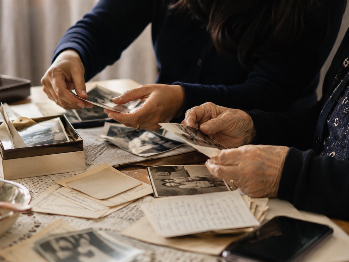 Two pairs of hands, one older, sorting through old photographs and handwritten letters on a table